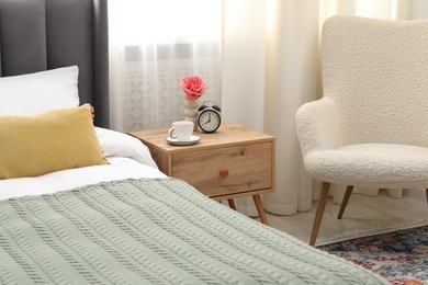 Photo of Bedside table with coffee, flower and alarm clock near bed indoors