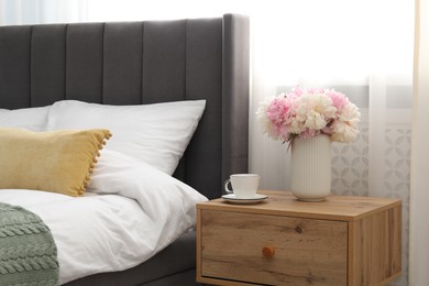 Photo of Bedside table with coffee and flowers near bed indoors