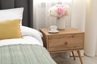 Photo of Bedside table with coffee and flowers near bed indoors