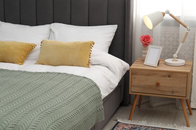 Photo of Bedside table with lamp, flower and frame near bed indoors