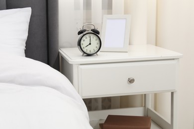 Photo of Bedside table with alarm clock and frame near bed indoors