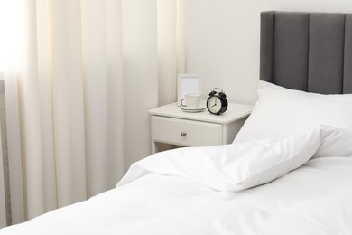 Photo of Bedside table with alarm clock, coffee and frame near bed indoors