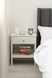 Photo of Bedside table with alarm clock, coffee and frame near bed indoors