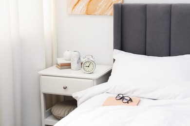 Photo of Bedside table with alarm clock and decor near bed indoors