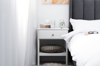 Photo of Bedside table with alarm clock and decor near bed indoors