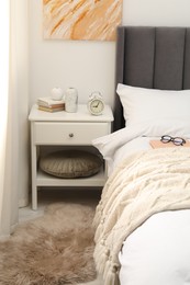 Photo of Bedside table with alarm clock and decor near bed indoors