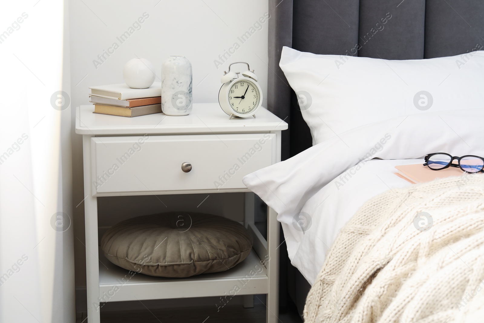 Bedside table with alarm clock and decor near bed indoors Photo of Bedside table with alarm clock and decor near bed indoors