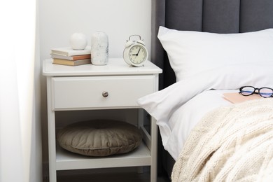 Photo of Bedside table with alarm clock and decor near bed indoors