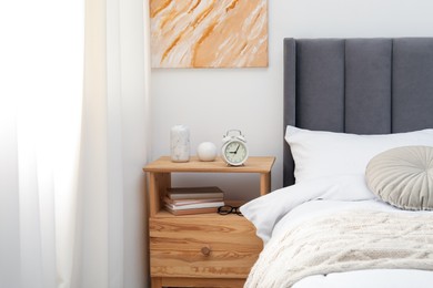 Photo of Bedside table with alarm clock and decor near bed indoors