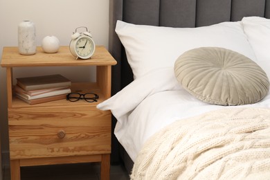 Photo of Bedside table with alarm clock and decor near bed indoors