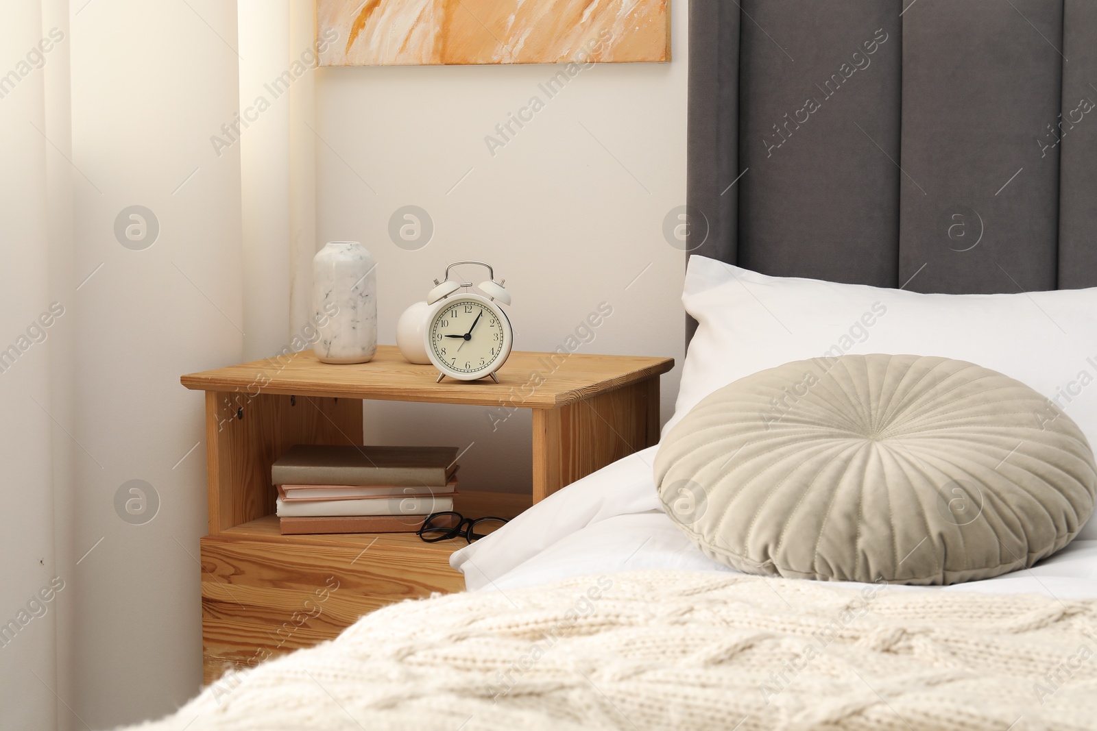 Bedside table with alarm clock and decor near bed indoors Photo of Bedside table with alarm clock and decor near bed indoors
