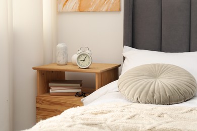 Photo of Bedside table with alarm clock and decor near bed indoors