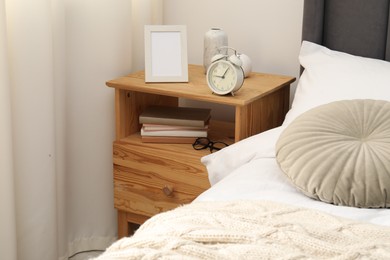 Photo of Bedside table with alarm clock and decor near bed indoors