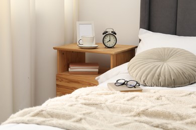 Photo of Bedside table with alarm clock, coffee and frame near bed indoors