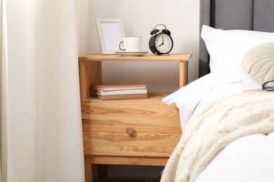 Photo of Bedside table with alarm clock, coffee and frame near bed indoors