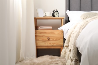 Photo of Bedside table with alarm clock, coffee and frame near bed indoors