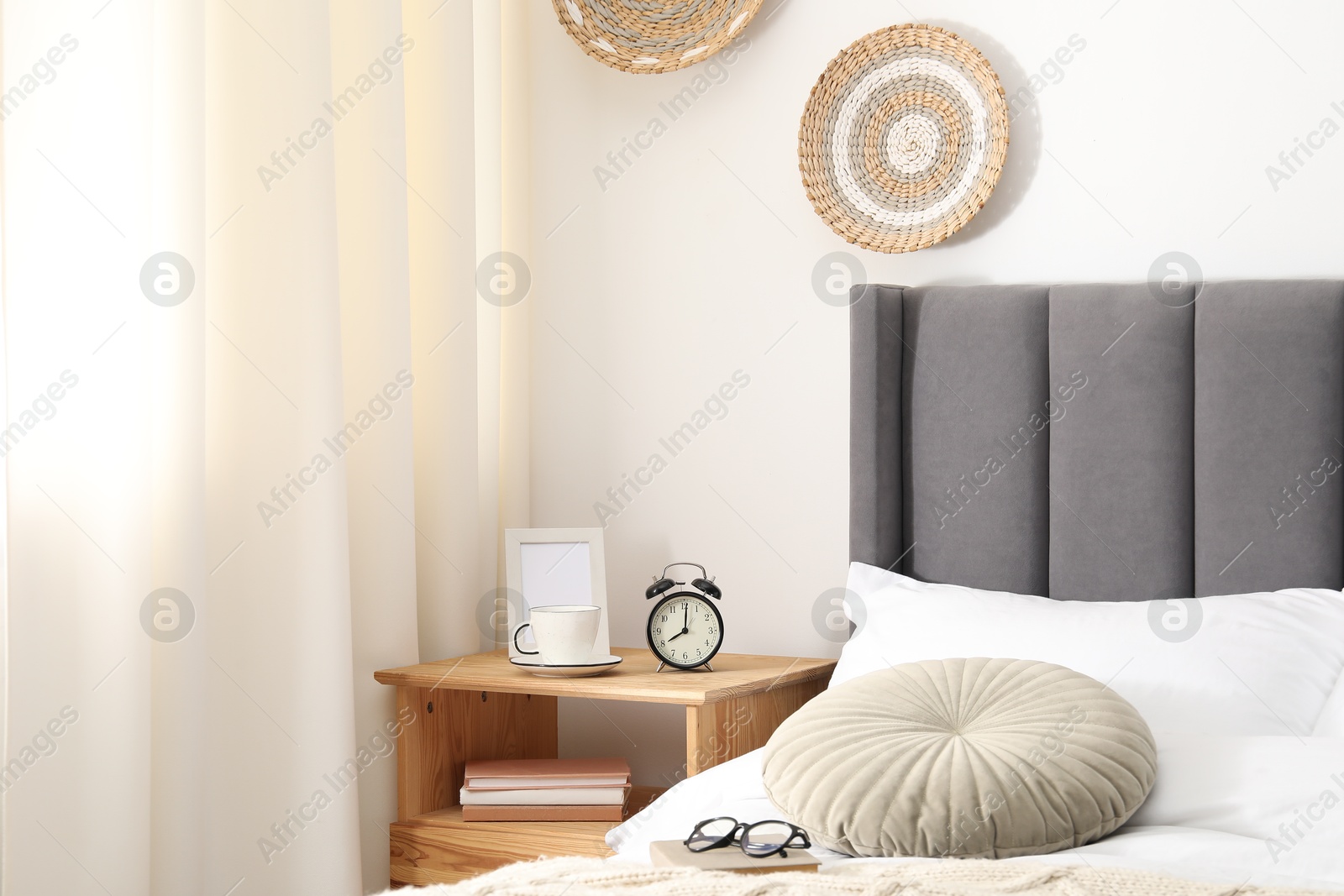 Bedside table with alarm clock, coffee and frame near bed indoors Photo of Bedside table with alarm clock, coffee and frame near bed indoors