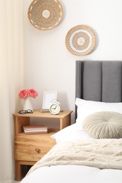 Photo of Bedside table with alarm clock, flowers and decor near bed indoors