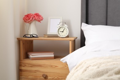 Photo of Bedside table with alarm clock, flowers and decor near bed indoors