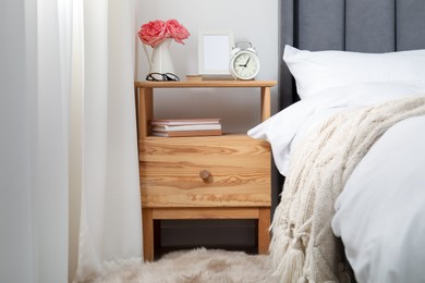 Photo of Bedside table with alarm clock, flowers and decor near bed indoors