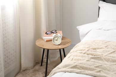 Photo of Bedside table with alarm clock, books and glasses near bed indoors