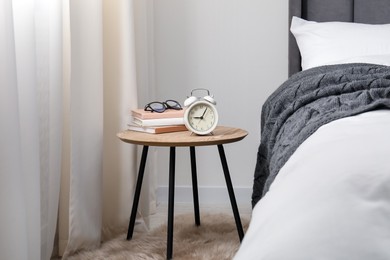 Photo of Bedside table with alarm clock, books and glasses near bed indoors