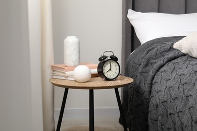 Photo of Bedside table with alarm clock and decor near bed indoors