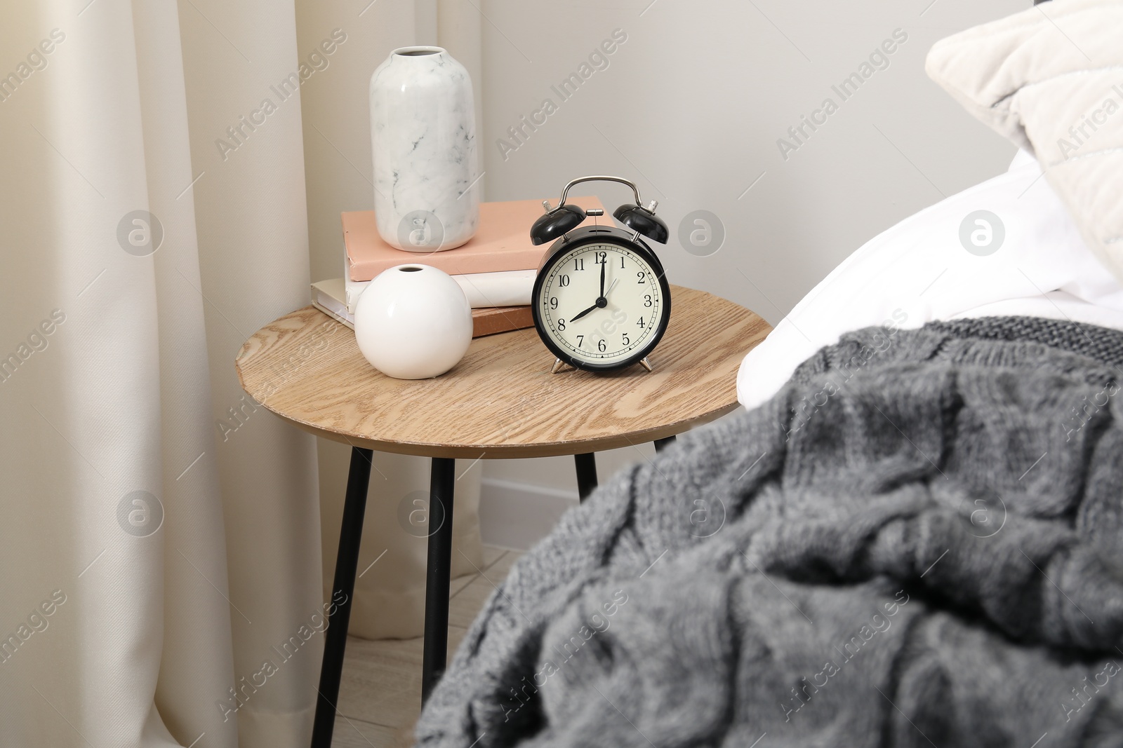 Bedside table with alarm clock and decor near bed indoors Photo of Bedside table with alarm clock and decor near bed indoors