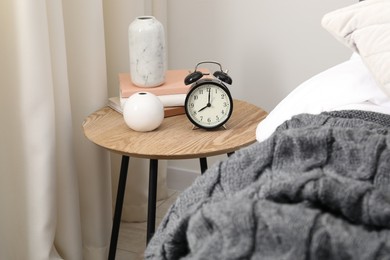 Photo of Bedside table with alarm clock and decor near bed indoors
