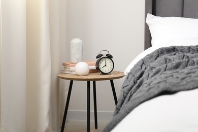 Photo of Bedside table with alarm clock and decor near bed indoors