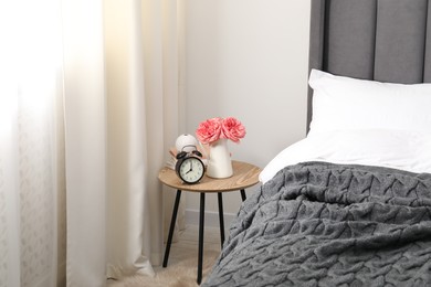 Photo of Bedside table with alarm clock, flowers and books near bed indoors