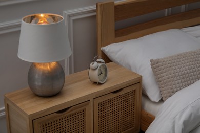 Photo of Bedside table with lamp and alarm clock near bed indoors