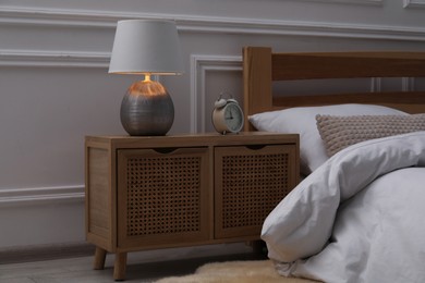 Photo of Bedside table with lamp and alarm clock near bed indoors
