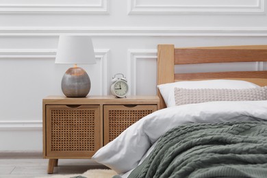 Photo of Bedside table with lamp and alarm clock near bed indoors