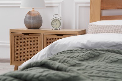 Photo of Bedside table with lamp and alarm clock near bed indoors