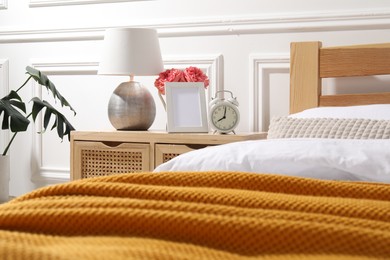 Photo of Bedside table with lamp, alarm clock and flowers near bed indoors