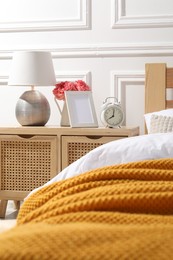 Photo of Bedside table with lamp, alarm clock and flowers near bed indoors