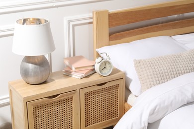 Photo of Bedside table with lamp, alarm clock and books near bed indoors