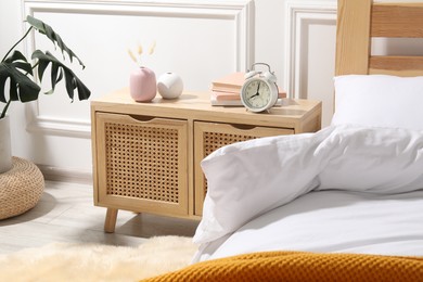 Photo of Bedside table with alarm clock, books and decor near bed indoors