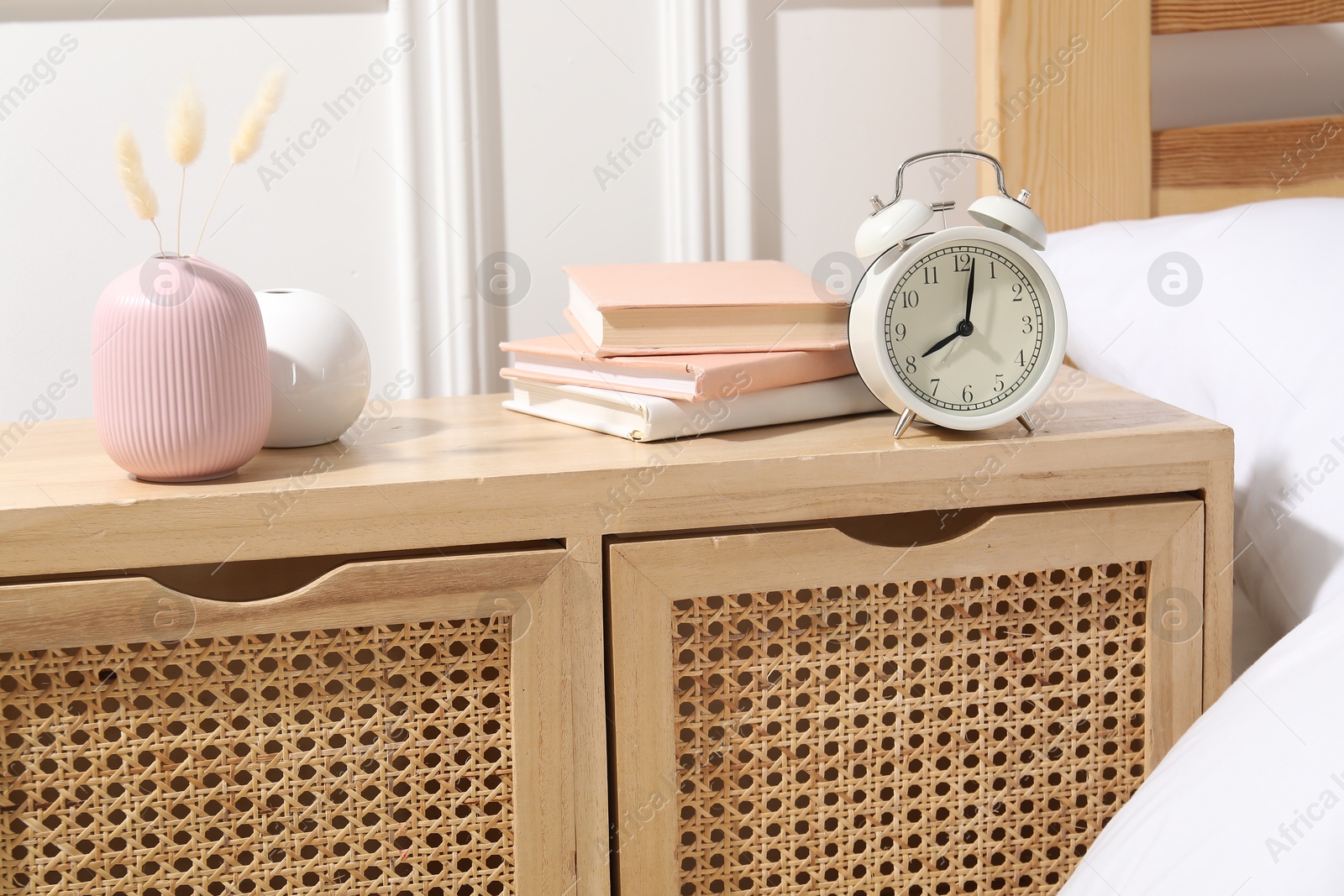 Bedside table with alarm clock, books and decor near bed indoors Photo of Bedside table with alarm clock, books and decor near bed indoors