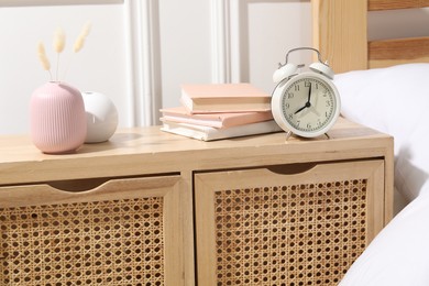 Photo of Bedside table with alarm clock, books and decor near bed indoors