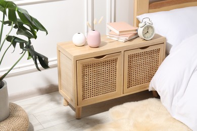 Photo of Bedside table with alarm clock, books and decor near bed indoors