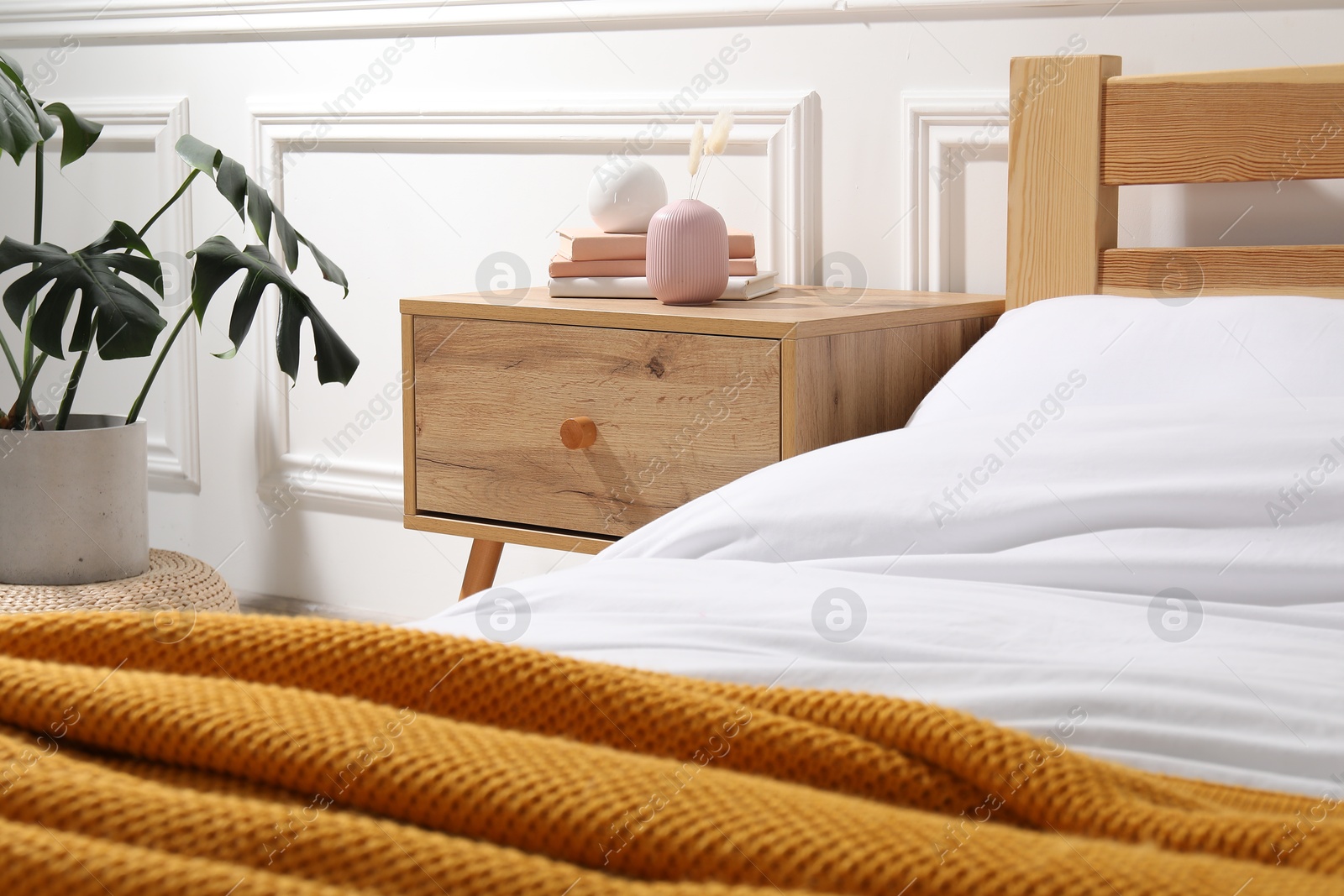 Bedside table with books and decor near bed indoors Photo of Bedside table with books and decor near bed indoors
