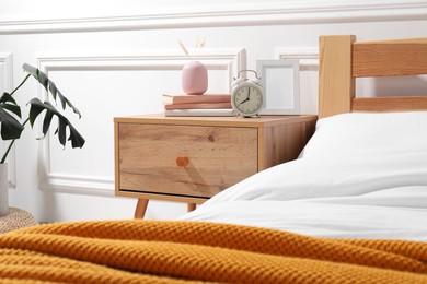 Photo of Bedside table with alarm clock, books and decor near bed indoors