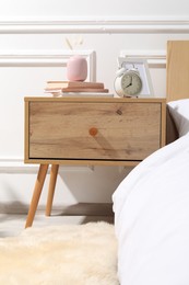 Photo of Bedside table with alarm clock, books and decor near bed indoors