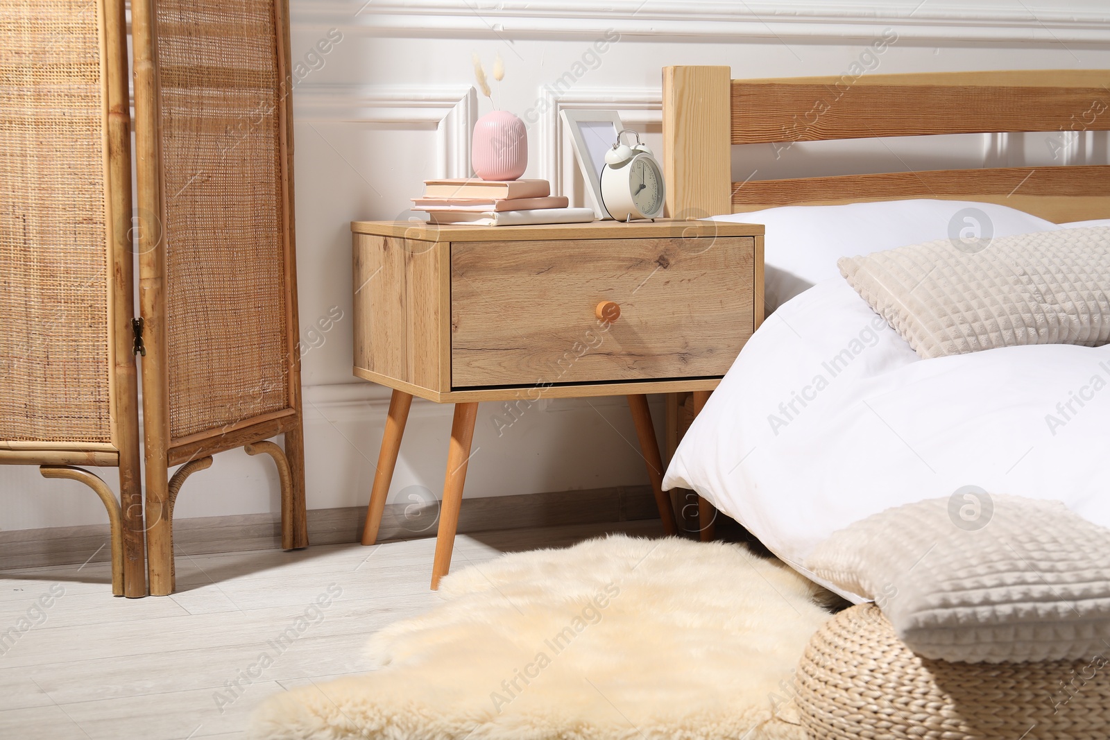 Bedside table with alarm clock, books and decor near bed indoors Photo of Bedside table with alarm clock, books and decor near bed indoors
