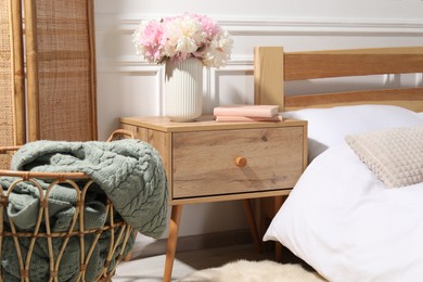 Photo of Bedside table with books and flowers near bed indoors