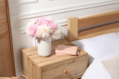 Photo of Bedside table with books and flowers near bed indoors