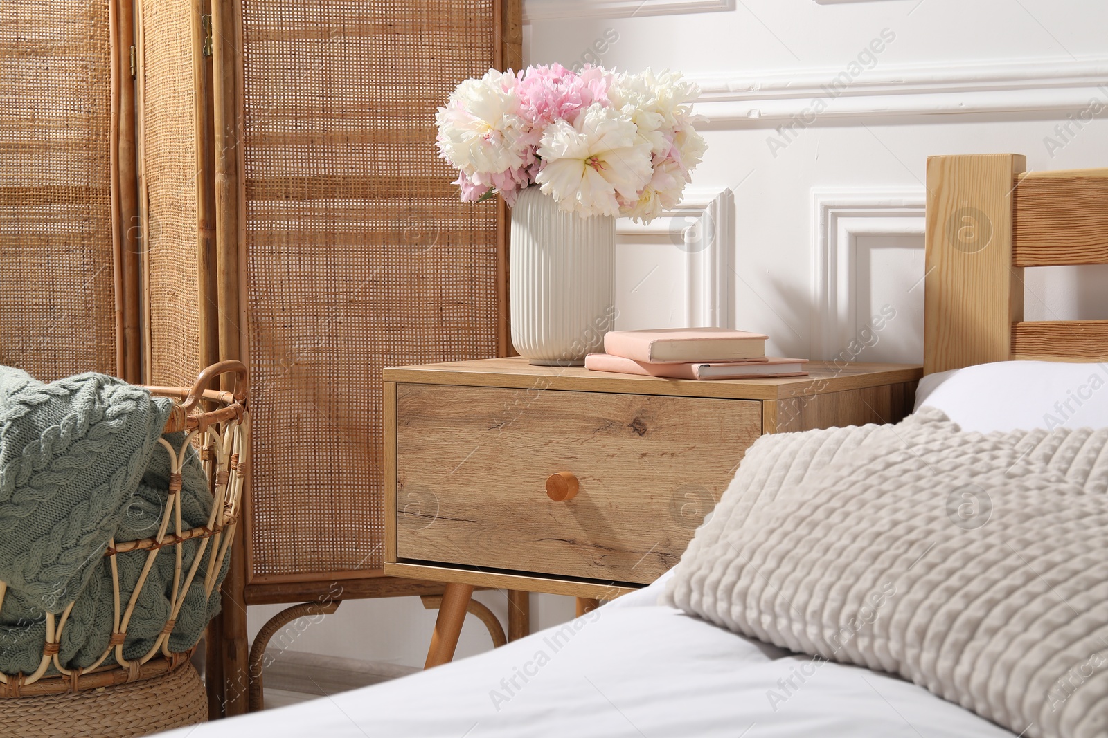 Bedside table with books and flowers near bed indoors Photo of Bedside table with books and flowers near bed indoors