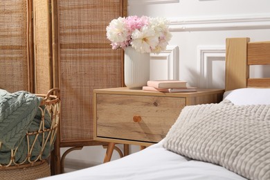 Photo of Bedside table with books and flowers near bed indoors